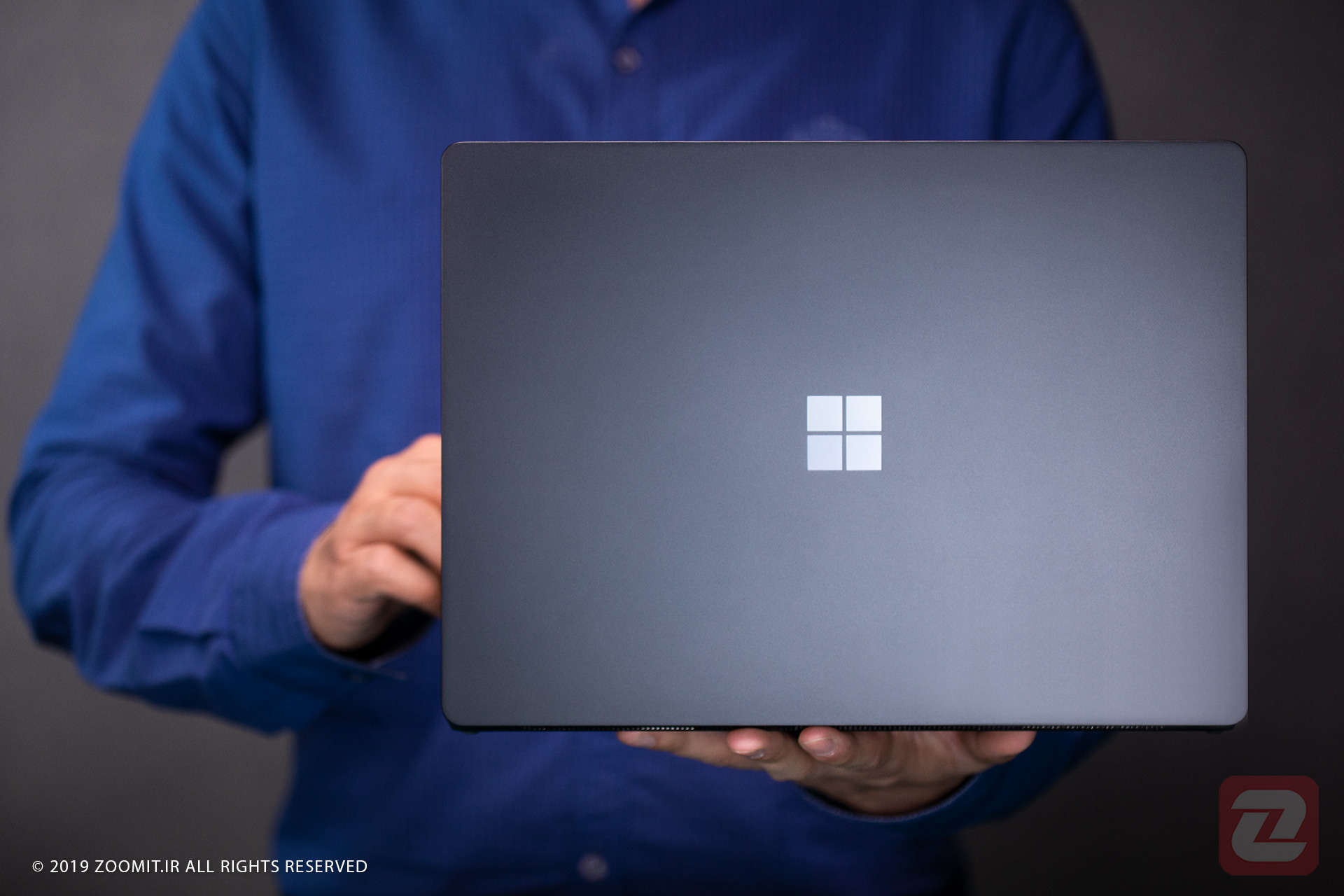 پشت سرفیس لپ تاپ 2 مایکروسافت رنگ خاکستری در دست فردی با لباس آبی