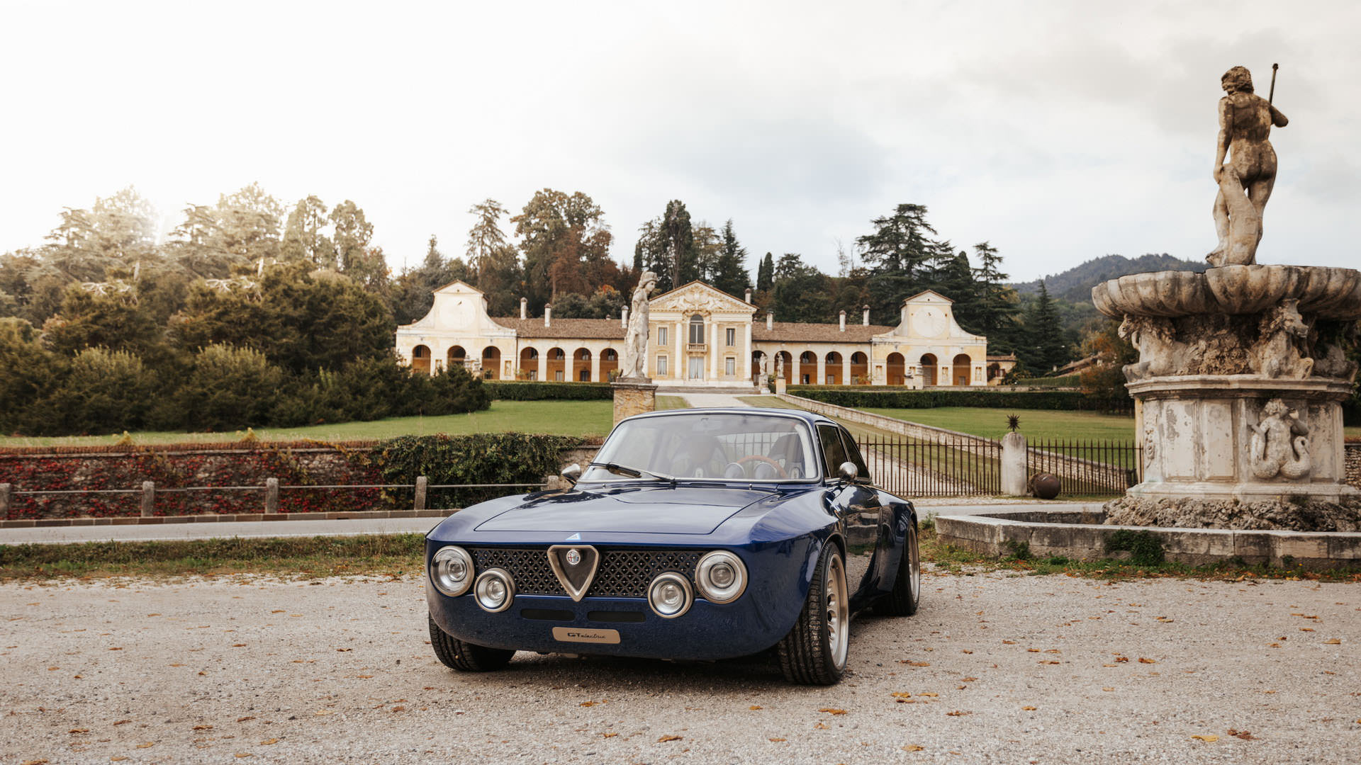 نمای جلو خودروی الکتریکی آلفا رومئو جولیا / Alfa Romeo Giulia GTA آبی رنگ در کنار ساختمان