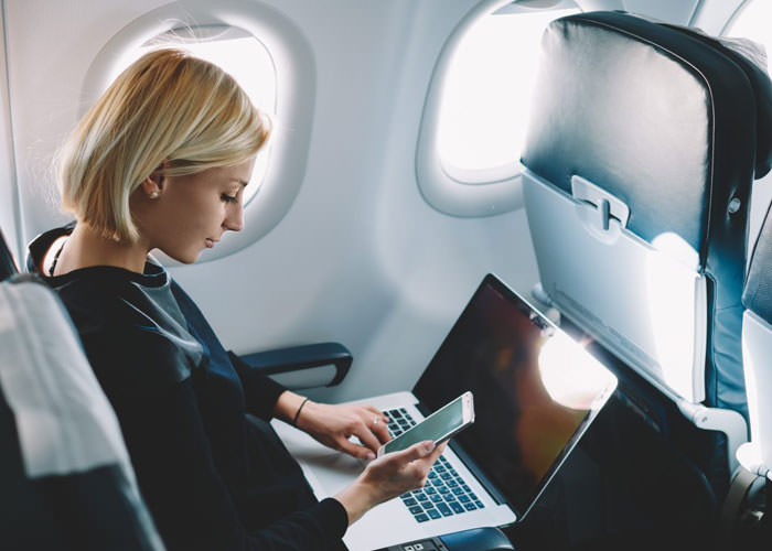 مسافر هواپیما در حال استفاده از وای-فای هواپیما با گوشی و لپ‌تاپ