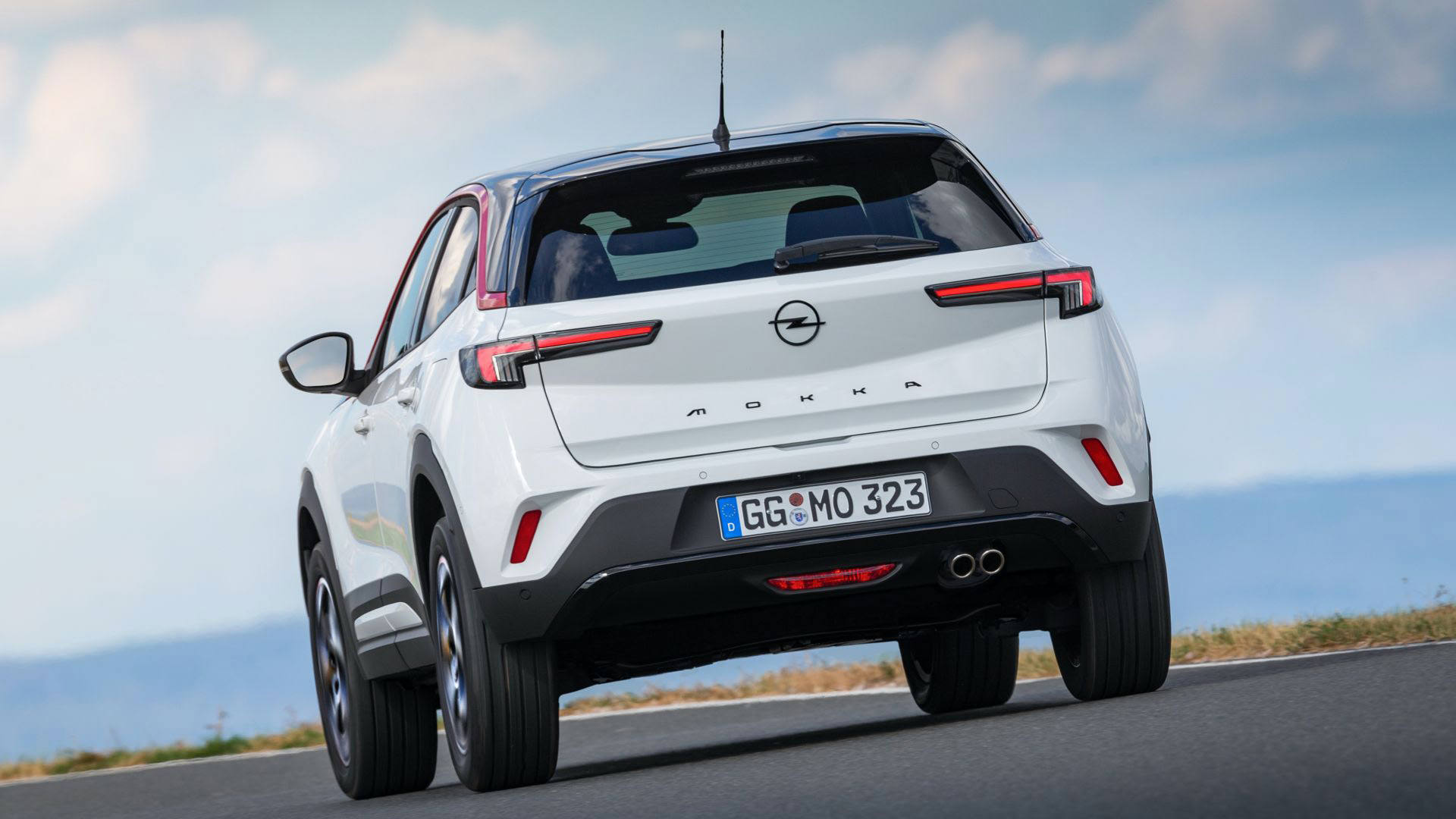 نمای عقب کراس اور کامپکت اوپل موکا 2021 / Opel Mokka با طرح دو رنگ سفید و مشکی در جاده با منظره آسمان آبی